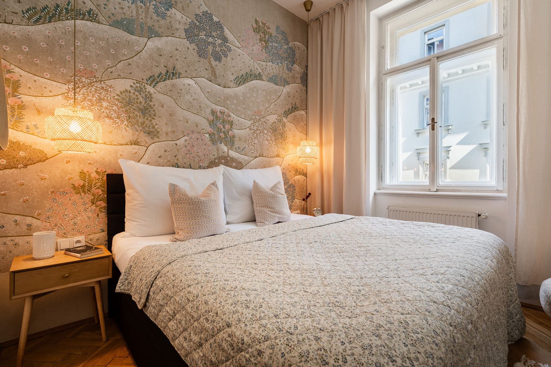 Cozy bedroom in a Prague period apartment with landscape mural wallpaper, pendant lamps and a tall double window