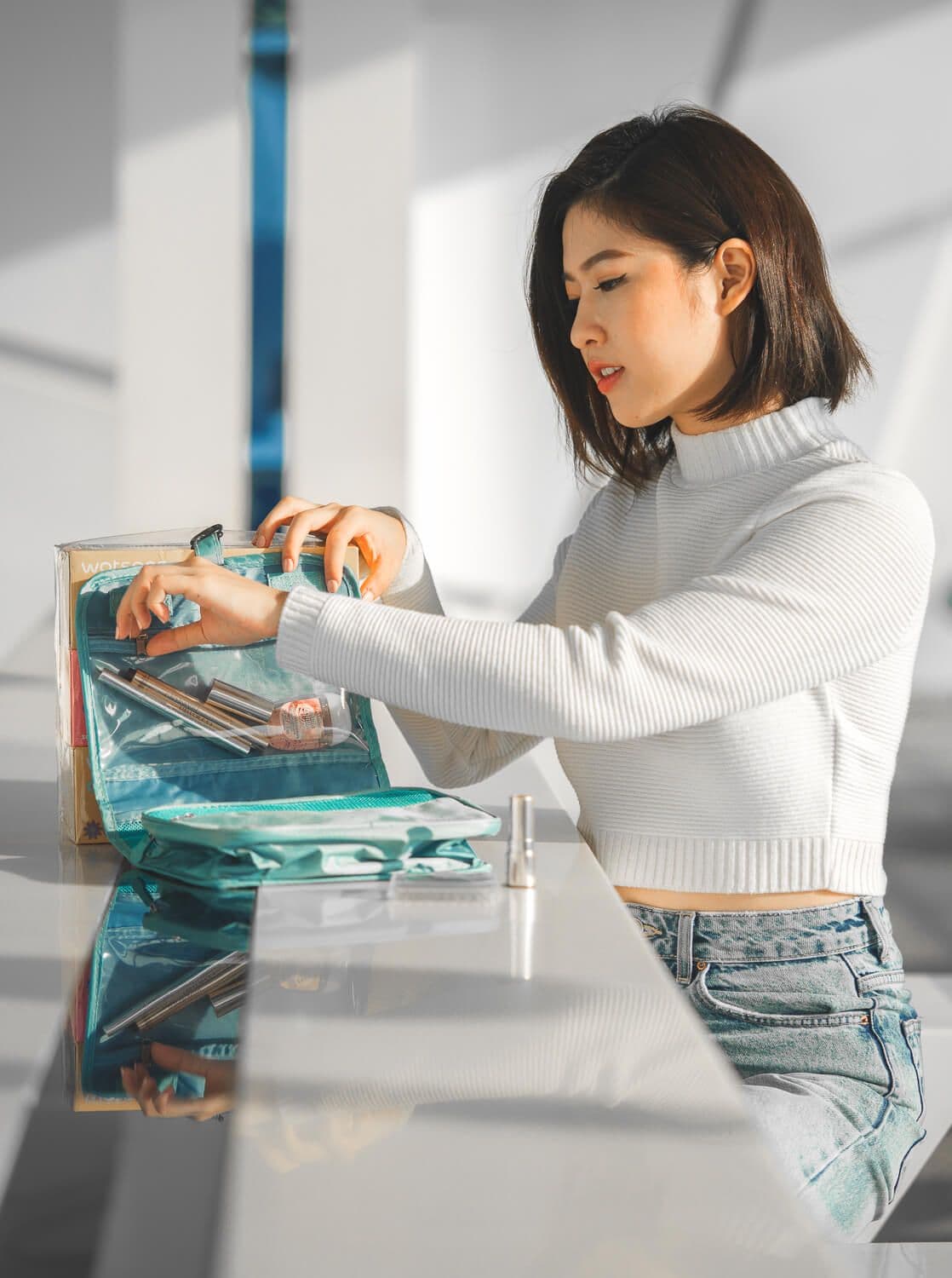 Bella Kuan packing cosmetics into a teal travel organiser, Watsons boxes beside her.