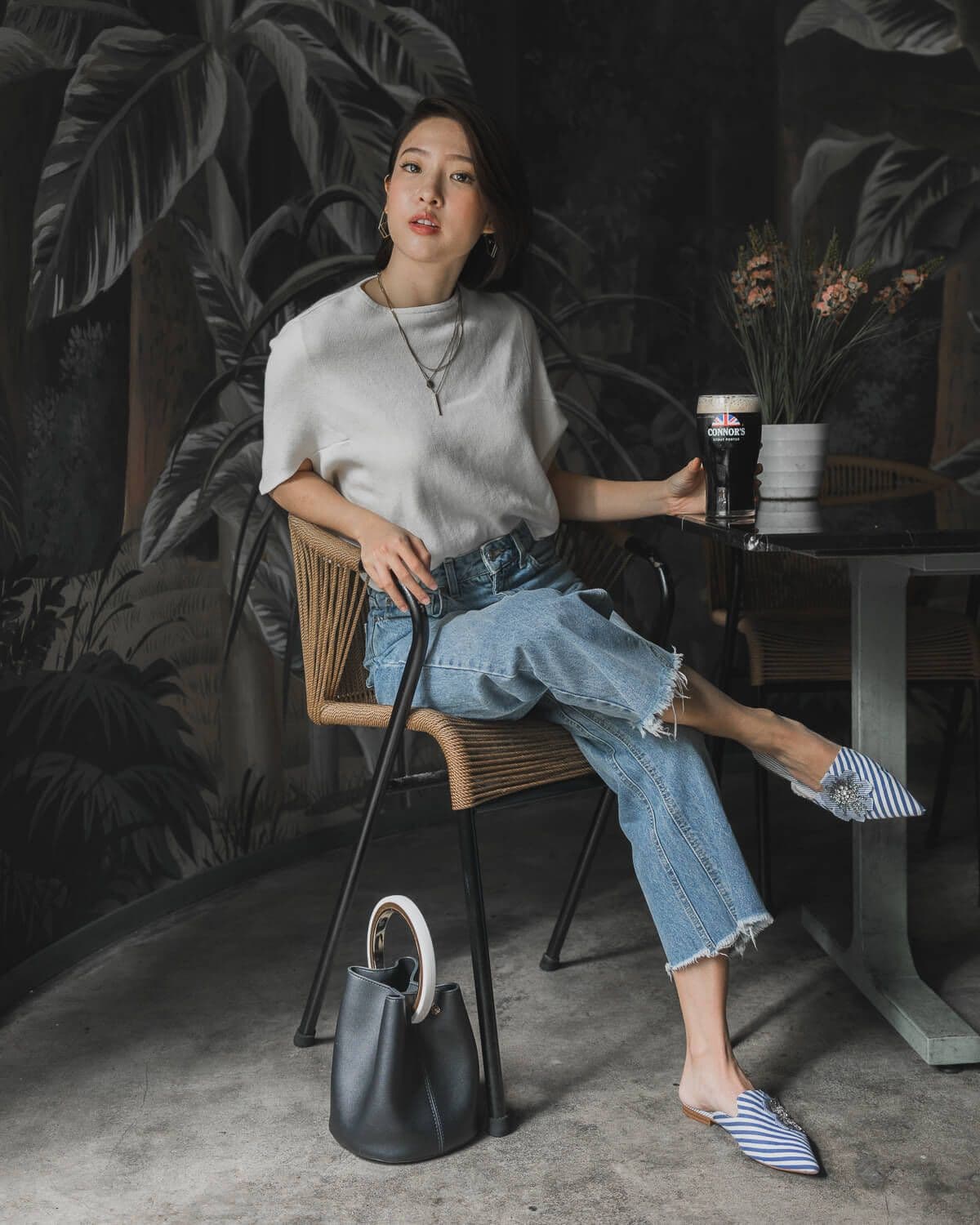 Bella Kuan on a rattan chair at a marble table with a glass of Connor’s stout, a dark jungle mural behind her.