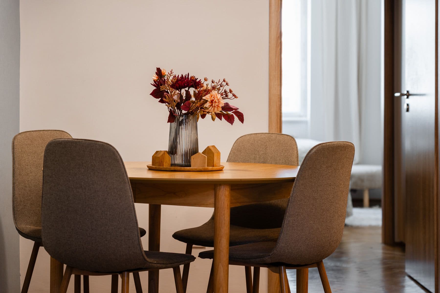 Autumn bouquet in a ribbed glass vase with small wooden house figurines on a round oak dining table