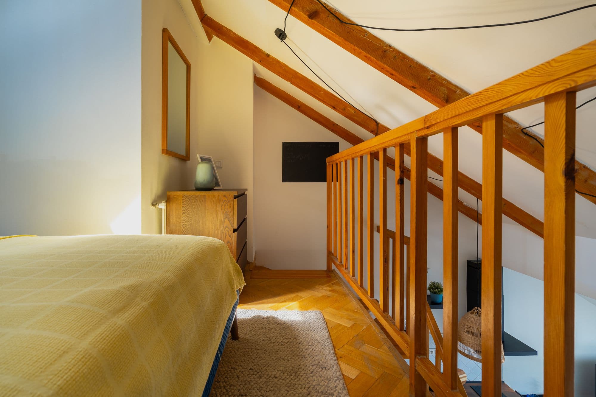 Bed with a blue velvet headboard, mustard and navy cushions and a Bauhaus exhibition poster beneath a skylight