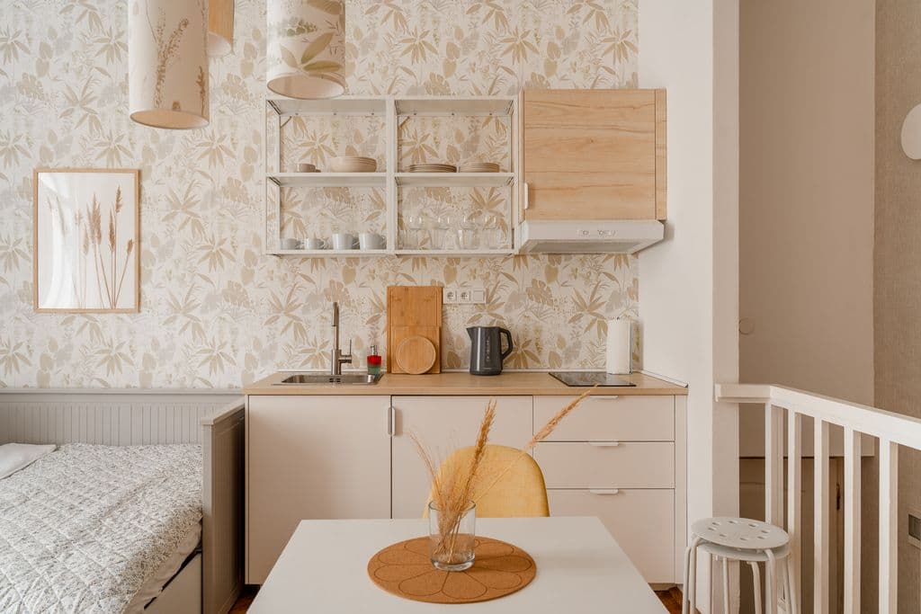 Cream kitchenette with open white shelving, a wood-look wall cabinet, kettle and hob under pendant lamps with botanical shades