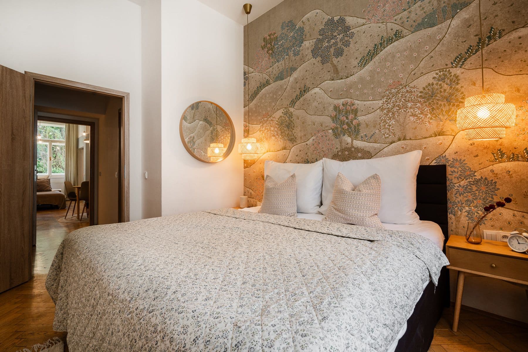 Bedroom with landscape mural wallpaper, rattan pendant lamps and a round mirror, with a view through to the living room