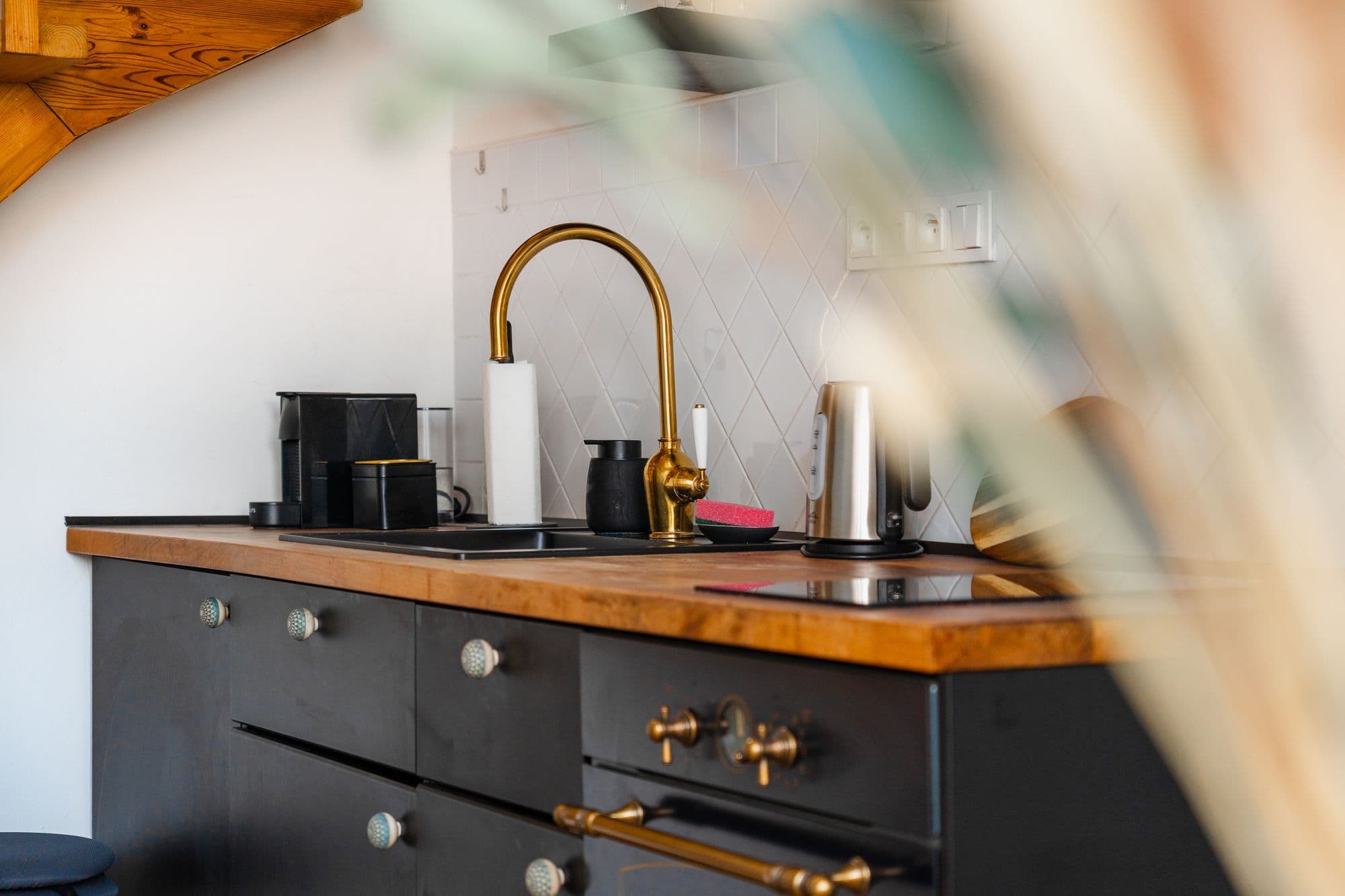 Brass gooseneck faucet, black sink and wooden countertop above black cabinets with a retro oven and ceramic knobs