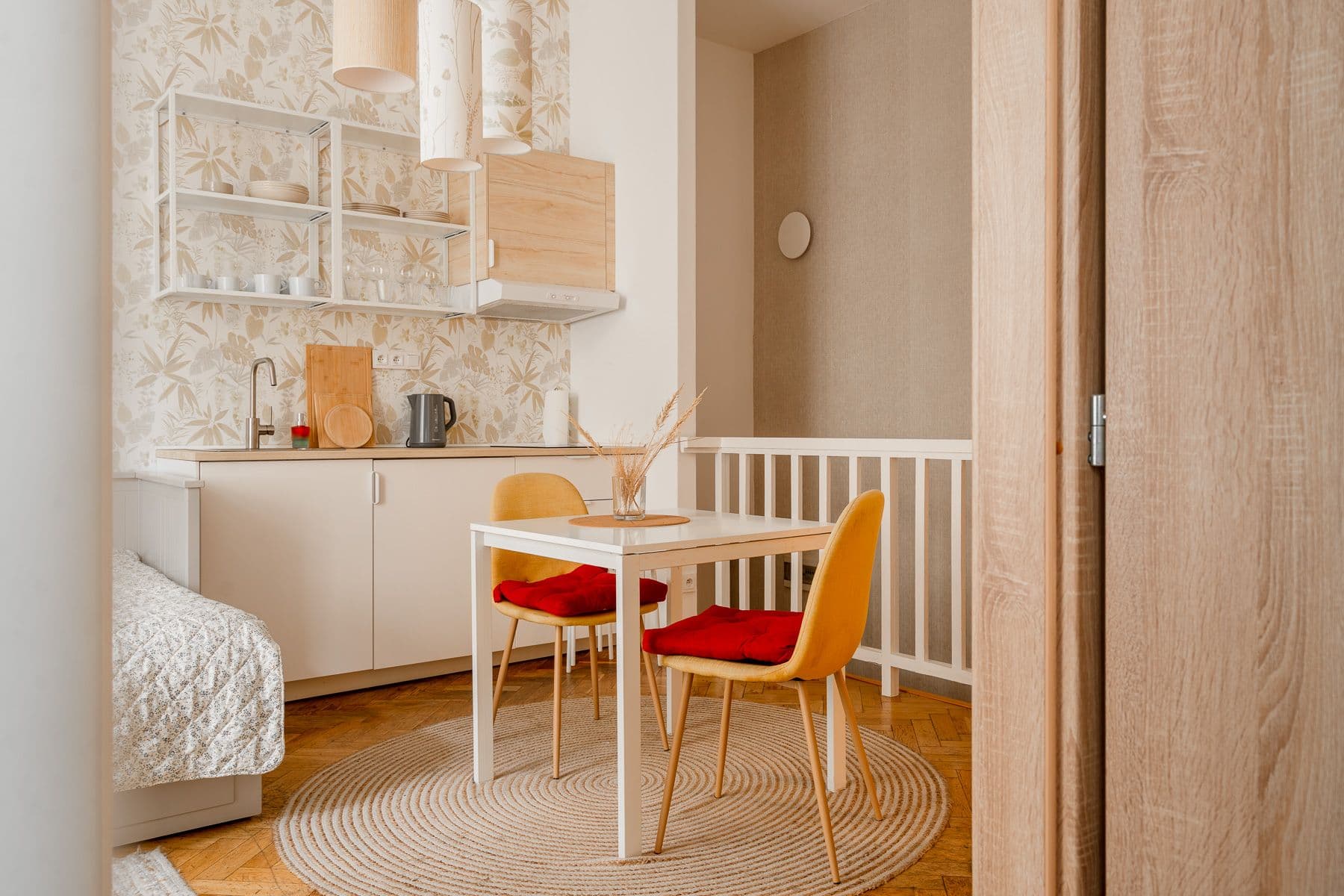 Dining nook with a white table, two mustard chairs with red seat cushions and a jute rug, beside a cream kitchenette