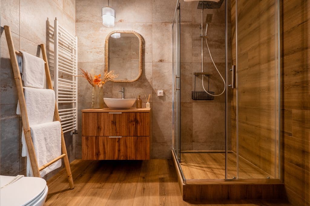 Warm-toned bathroom with a floating oak vanity, vessel sink, rattan mirror, glass shower and bamboo towel ladder